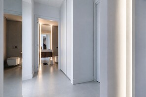 A modern hallway with a minimalist design, leading to a bathroom with a toilet and a sink.