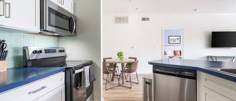 A modern kitchen with stainless steel appliances, a dining area with a table and chairs, and a small plant.