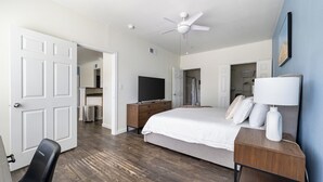 Een slaapkamer met een bed, een bureau, een stoel, een televisie en een plafondventilator.