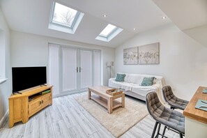 Una sala de estar moderna con televisor de pantalla plana, mueble de entretenimiento de madera, sofá blanco y un comedor con taburetes de bar.