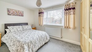 A bedroom with a bed, a nightstand, a radiator, a window with curtains, and a wall-mounted artwork. - One Bed in Guilden Sutton by Guestz (Guilden Sutton)
