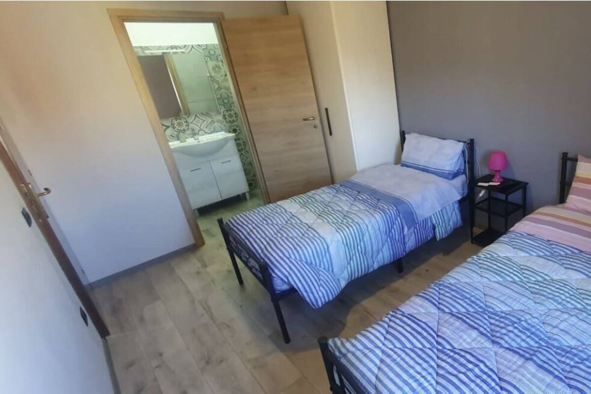 Ett sovrum med två sängar, en garderob och ett litet nattduksbord med en lampa.