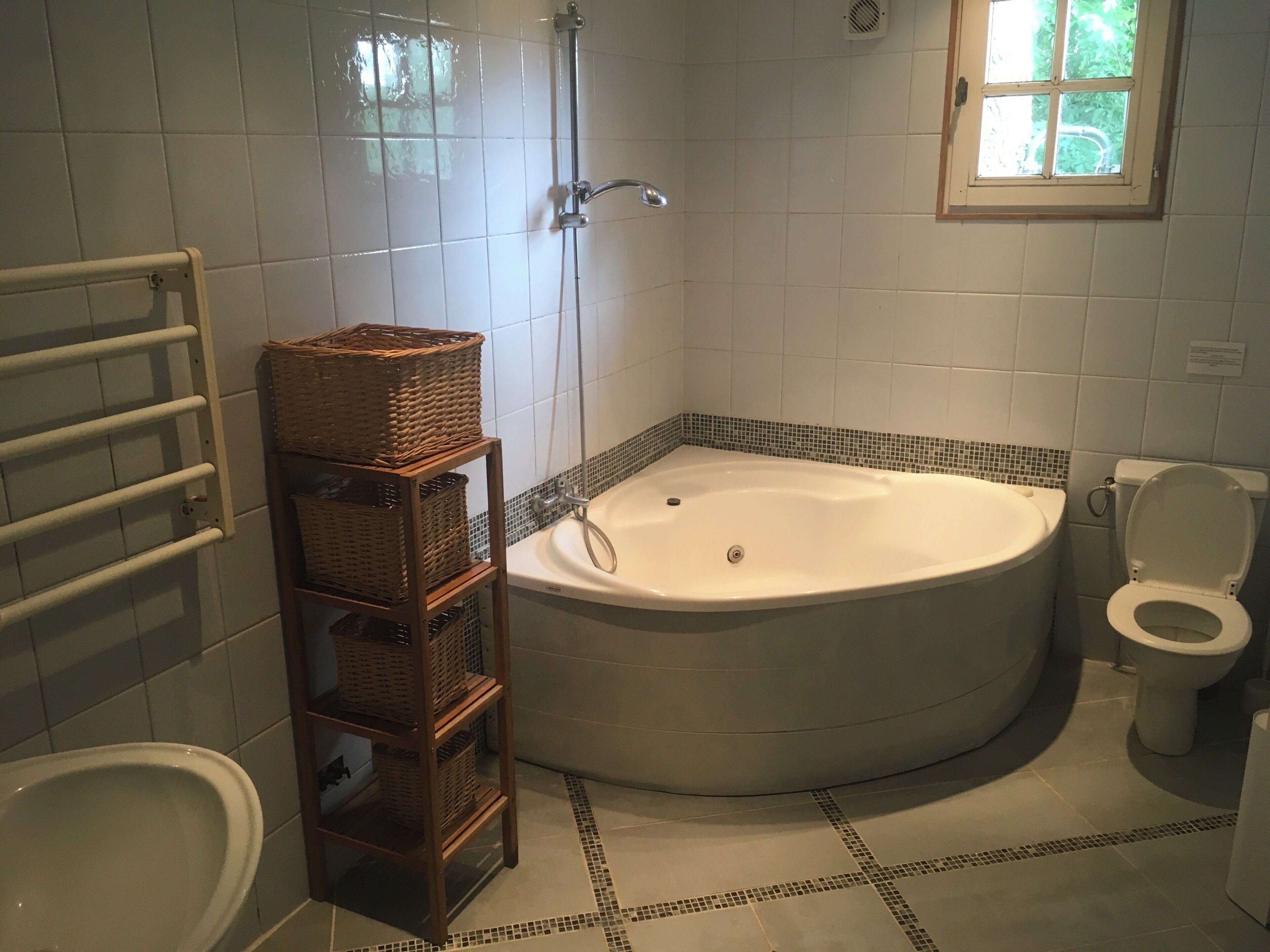 Ein Badezimmer mit Badewanne, Toilette und Dusche. Auf einem Regal stehen Körbe aus Weidengeflecht.