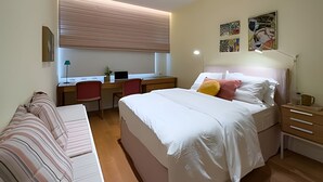 A bedroom with a bed, a desk, a chair, a bedside table, and a window with blinds. - Ipanema | Duplex no melhor local do bairro, 4 quartos, 5 min da Praia - por Casapē Rio (Rio de Janeiro)