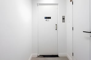 Une porte blanche avec une petite grille d’aération, un interphone et un lecteur de cartes magnétiques.