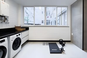 A compact kitchen with a washing machine, a window with a view of buildings, and a black exercise mat. - Ipanema | Duplex no melhor local do bairro, 4 quartos, 5 min da Praia - por Casapē Rio (Rio de Janeiro)