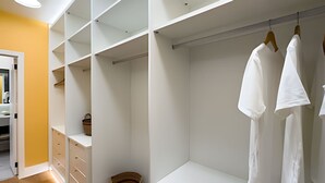 Un vestidor con estanterías abiertas, un banco y ropa colgada.