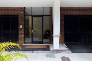A building entrance with a glass door, a brick wall, and a black door. - Ipanema | Duplex no melhor local do bairro, 4 quartos, 5 min da Praia - por Casapē Rio (Rio de Janeiro)