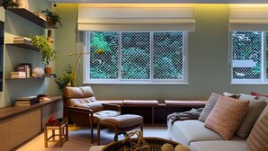 A living room with a sofa, a chair, a small table, and a window with a view of greenery. - Ipanema | Duplex no melhor local do bairro, 4 quartos, 5 min da Praia - por Casapē Rio (Rio de Janeiro)