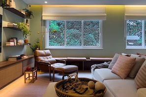 Ein Wohnzimmer mit einer Couch, einem Sessel, einem kleinen Tisch und einem Fenster mit Blick auf Grünflächen.