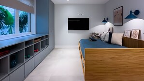 Un dormitorio moderno con cama, estanterías empotradas, televisor y ventana con vistas a zonas verdes.