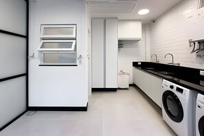 A modern kitchen with a washing machine, a sink, and a door with a window. - Ipanema | Duplex no melhor local do bairro, 4 quartos, 5 min da Praia - por Casapē Rio (Rio de Janeiro)