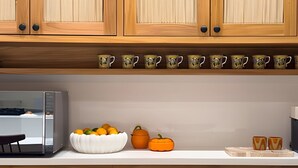Una cocina con armarios de madera, encimera blanca, un bol de fruta, una calabaza y una cafetera.