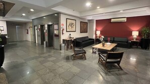 Um hall amplo com piso xadrez, um sofá preto, uma mesa de madeira com cadeiras e uma parede decorada em vermelho.