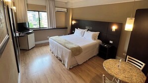 Una habitación de hotel con una cama, un escritorio con televisor, una mesita y una silla.