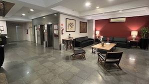 Un hall d’entrée spacieux avec un sol à carreaux, un canapé noir, une table en bois avec des chaises et un mur d’accent rouge.
