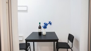 A small dining area with a table, two chairs, a bottle of wine, and a vase with blue flowers.