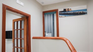 A hotel room with a wooden-framed door, a white sink, and a painting of a coastal scene on the wall.
