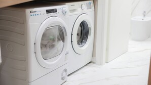 A front view of a Candy SmartPro front-loading washing machine in a bathroom with a white marble floor and a white sink in the background.