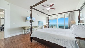 Une chambre spacieuse dotée d’un lit à baldaquin, d’un ventilateur de plafond et d’une grande fenêtre offrant une vue sur l’océan.