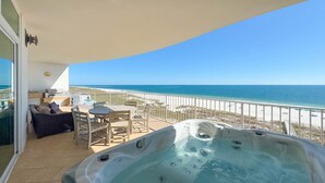 Un balcón con un jacuzzi, una mesa y sillas, con vistas a una playa y el océano.