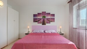 Ein Schlafzimmer mit einem großen Bett, zwei Nachttischen, einem Wandbild und einem Fenster mit Vorhängen.