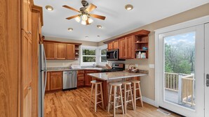 A modern kitchen with wooden cabinets, a built-in microwave, and a large island with stools. - Secluded Woodland Retreat Near Starved Rock Park 4 Bedroom Home (Ottawa)