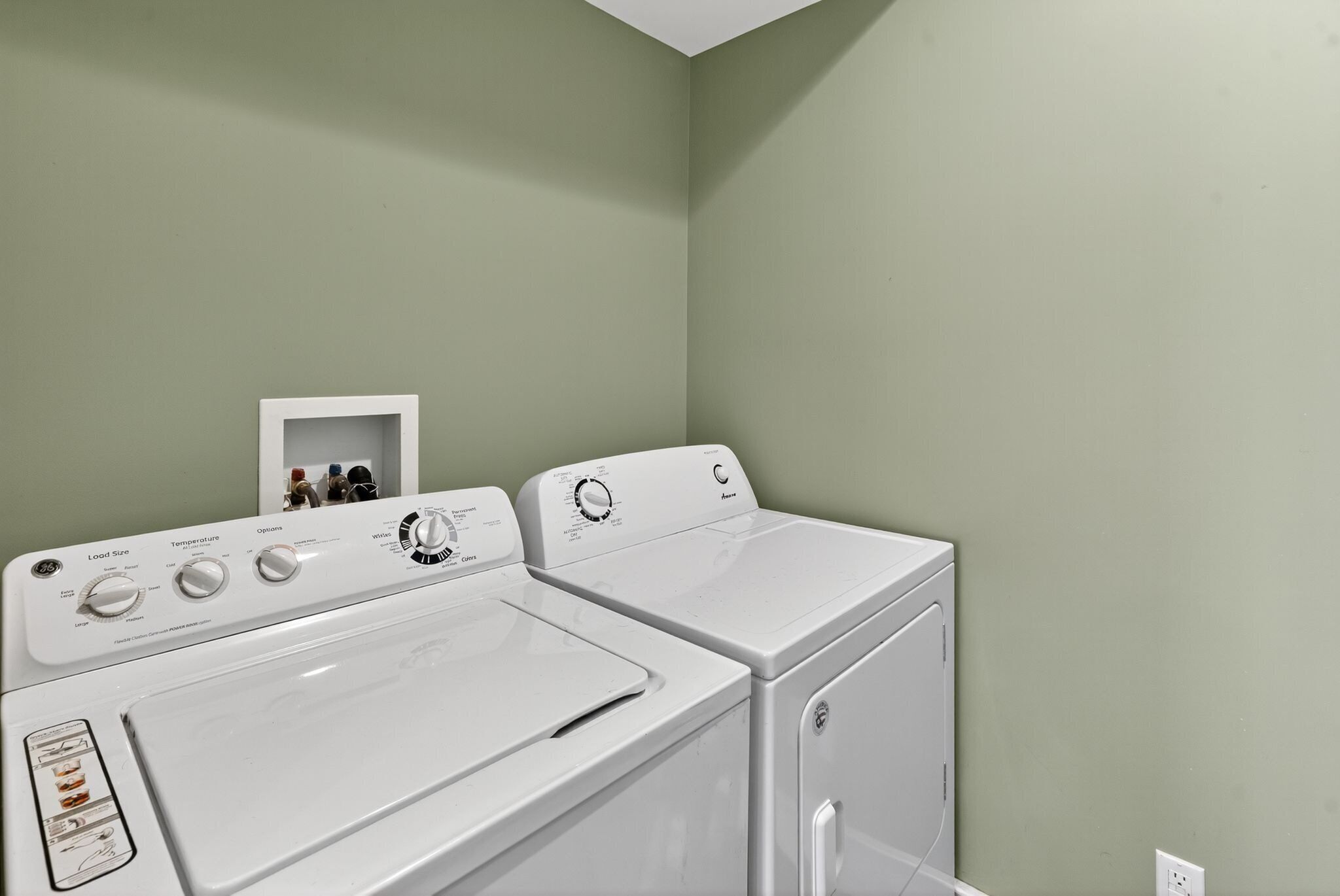 Un espace buanderie comprenant un lave-linge et un sèche-linge à chargement frontal, un panneau de commande avec différents réglages et une petite étagère contenant des produits de lessive.