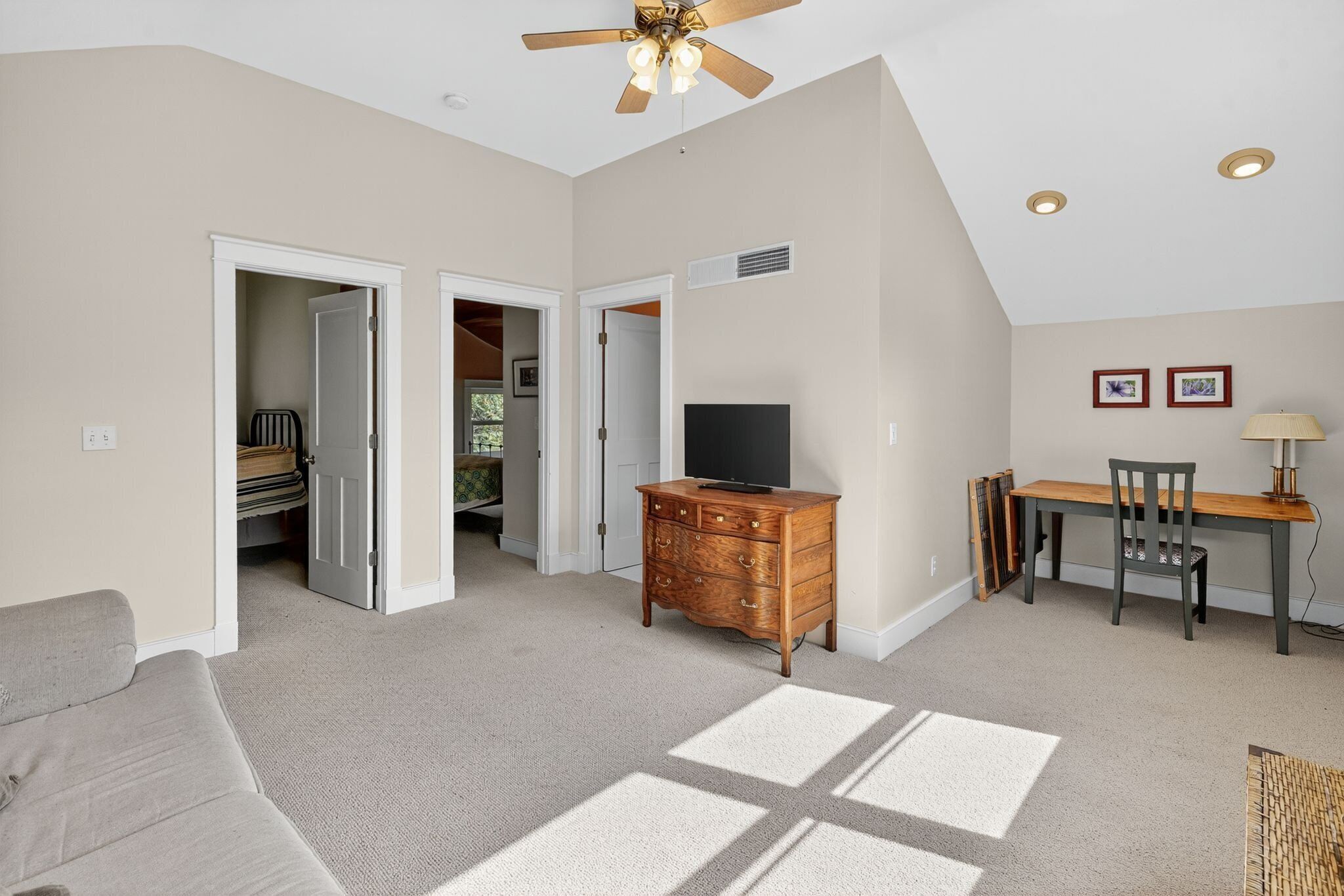A spacious room with a ceiling fan, a television on a wooden dresser, a dining table with chairs, and a sofa.