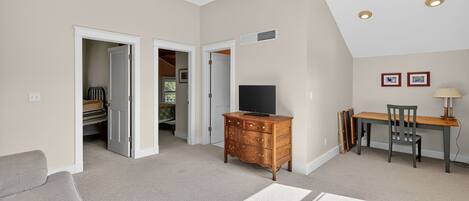 A spacious room with a ceiling fan, a television on a wooden dresser, a dining table with chairs, and a sofa.