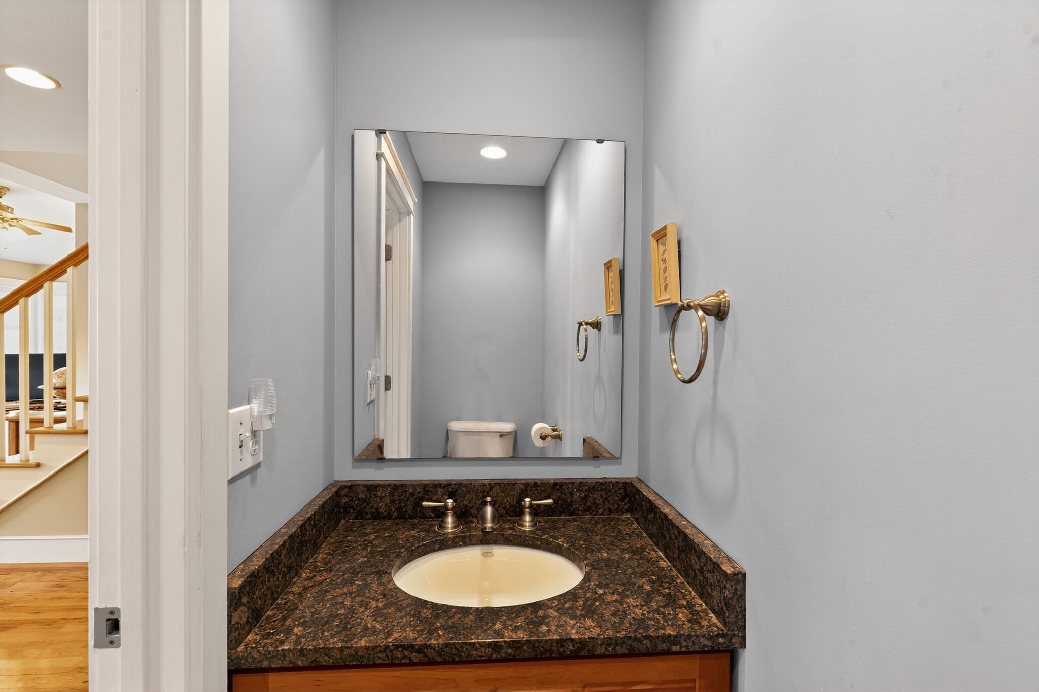 Un baño con lavamanos de encimera de granito, un espejo grande y un inodoro.