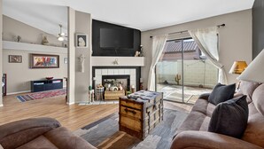 A living room with a fireplace, a television mounted above it, and a large window with curtains. - Chilled Tempe Oasis Shaded BBQ Lounge Near ASU 2 Bedroom Home (Tempe)