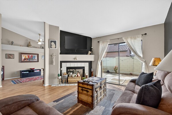 A living room with a fireplace, a television mounted above it, and a large window with curtains. - Chilled Tempe Oasis Shaded BBQ Lounge Near ASU 2 Bedroom Home (Tempe)