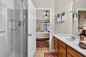 A modern bathroom with a glass shower door, a white sink, wooden cabinets, and a ceiling fan. - Chilled Tempe Oasis Shaded BBQ Lounge Near ASU 2 Bedroom Home (Tempe)