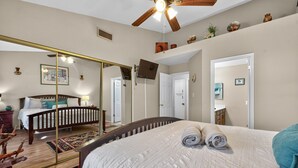 A bedroom with a large bed, a ceiling fan, a mirror, and a view of the bathroom. - Chilled Tempe Oasis Shaded BBQ Lounge Near ASU 2 Bedroom Home (Tempe)