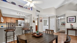 A spacious dining area with a wooden table and chairs, a ceiling fan, and a kitchen area with wooden cabinets and a refrigerator. - Chilled Tempe Oasis Shaded BBQ Lounge Near ASU 2 Bedroom Home (Tempe)