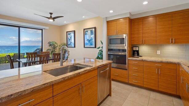 A modern kitchen with wooden cabinets, stainless steel appliances, and a view of the ocean. - Makena Surf, #f-111 2 Bedroom Condo (Kihei)