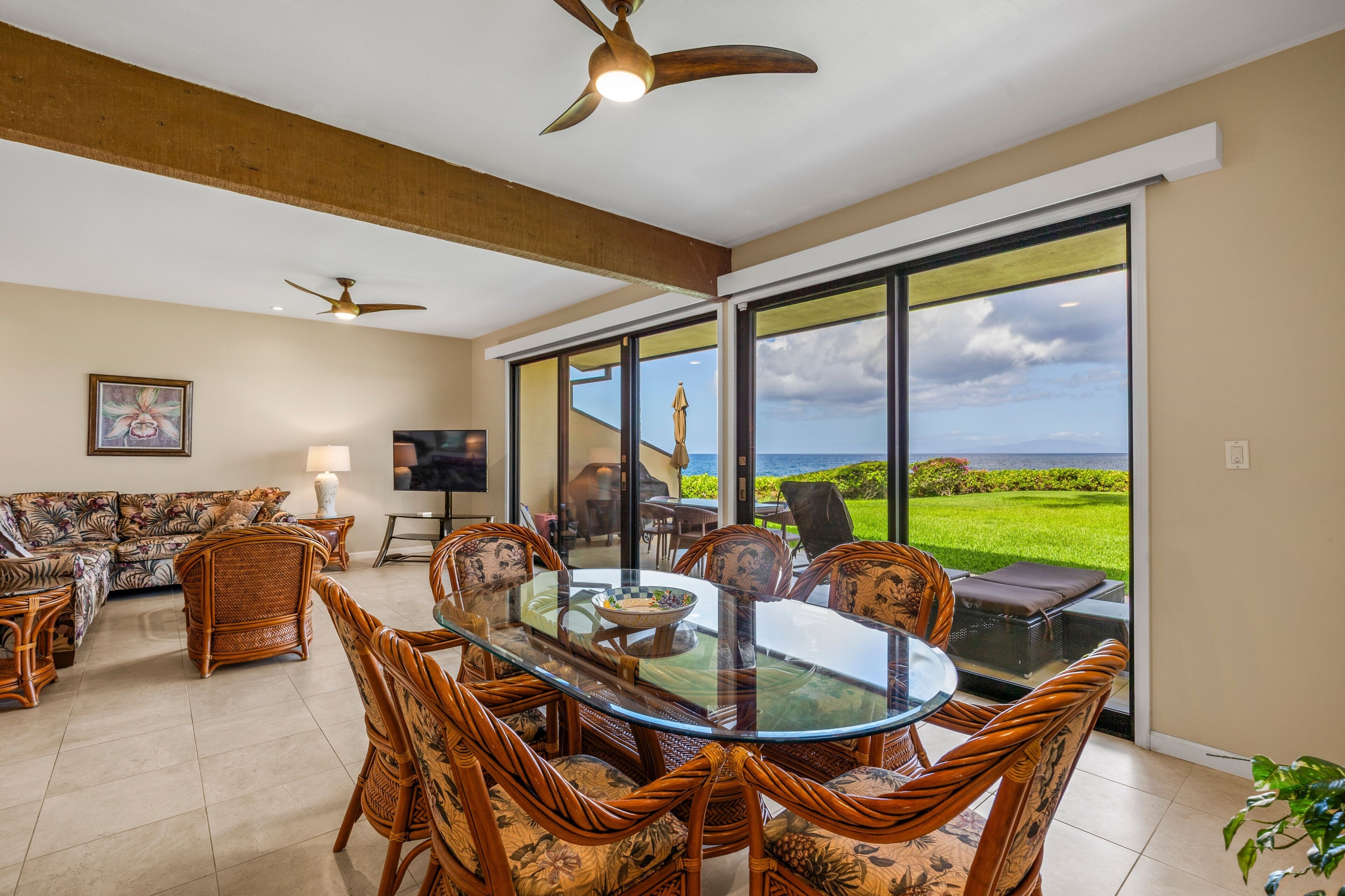 A spacious living area with a glass dining table surrounded by wicker chairs, a sofa, and a television.