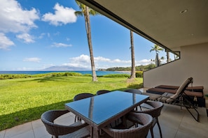 An outdoor patio with a view of the ocean, a table with chairs, and a lounge area. - Makena Surf, #f-109 2 Bedroom Condo (Kihei)