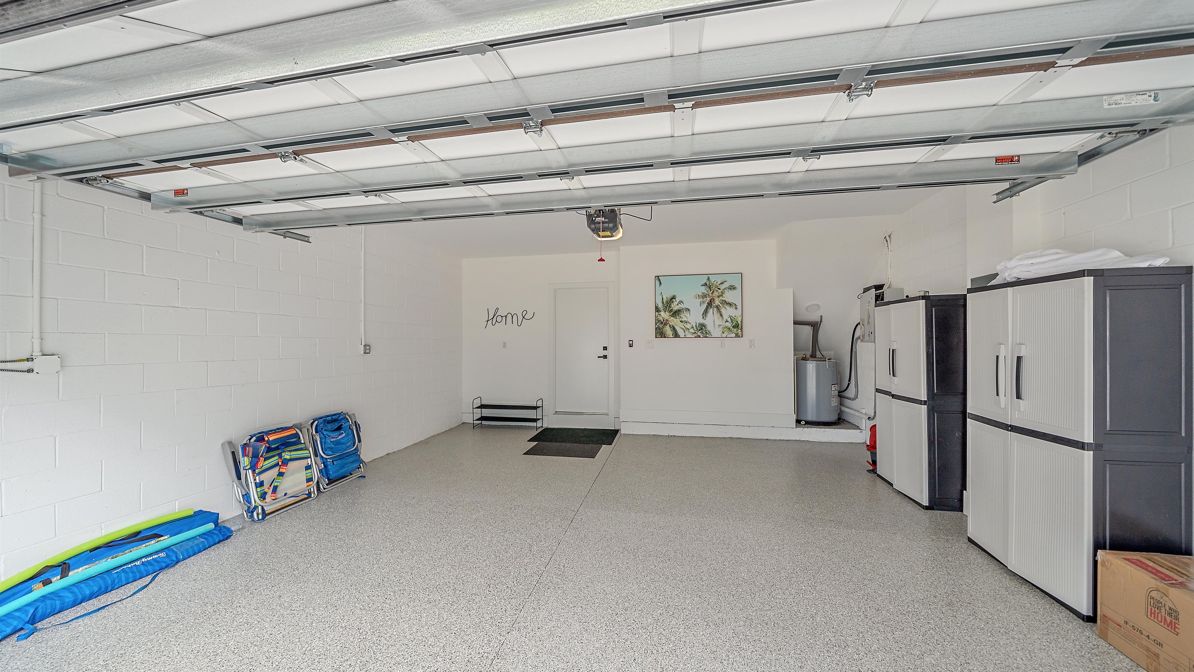 A clean, well-lit garage with a white door labeled "Home," a water heater, and a refrigerator.