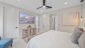 Ein Schlafzimmer mit einem Bett, einem Deckenventilator, einem an der Wand befestigten Fernseher, einer Kommode und einem Gemälde.