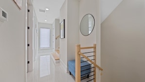 Un pasillo con una escalera de madera, un banco azul y un espejo en la pared.