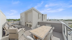 Una terraza en la azotea con mesa de madera, mobiliario de mimbre, una parrilla y vistas a la ciudad.