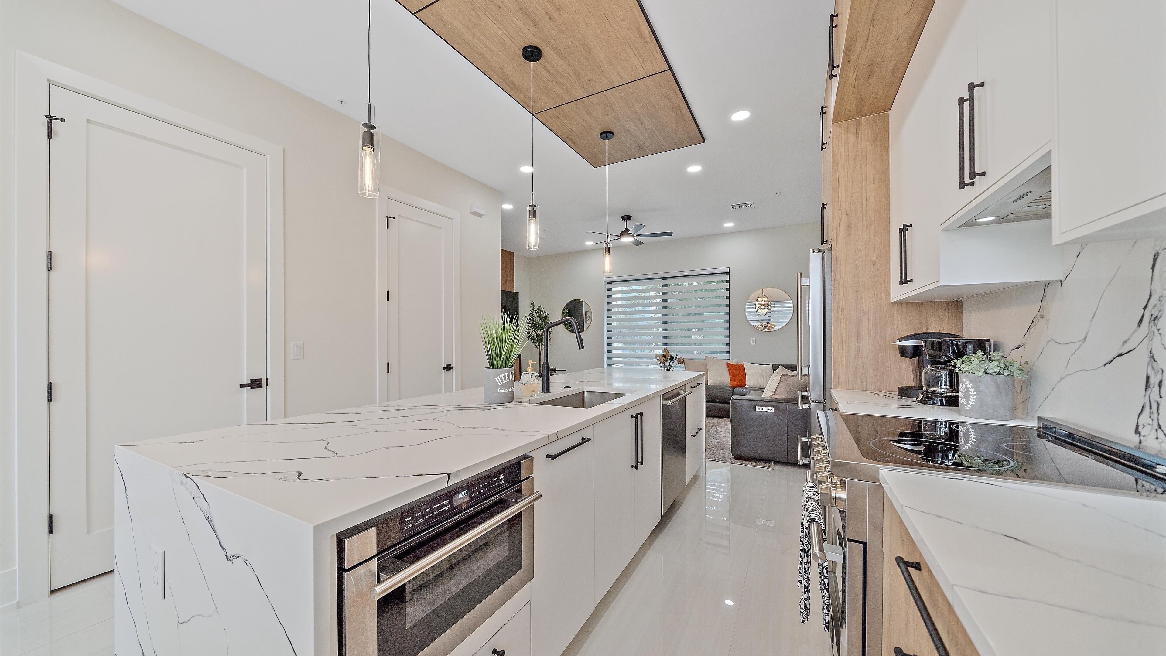 Una cocina moderna con armarios blancos, una isla central con horno integrado, iluminación colgante y techo de madera.