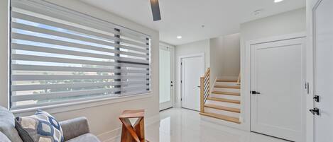 A modern living room with a large window, a ceiling fan, and a staircase leading to another level.