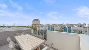 Eine Dachterrasse mit Holztisch und Korbstühlen mit Blick auf moderne Gebäude und einen klaren Himmel.
