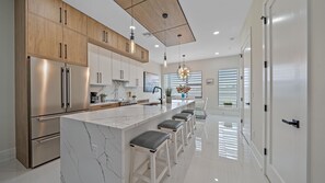 Cocina moderna con isla de mármol, electrodomésticos de acero inoxidable, armarios de madera y una lámpara colgante.