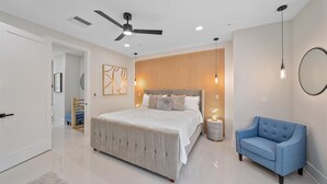Un dormitorio con una cama grande, un ventilador de techo, un sillón azul y una pared de paneles de madera.