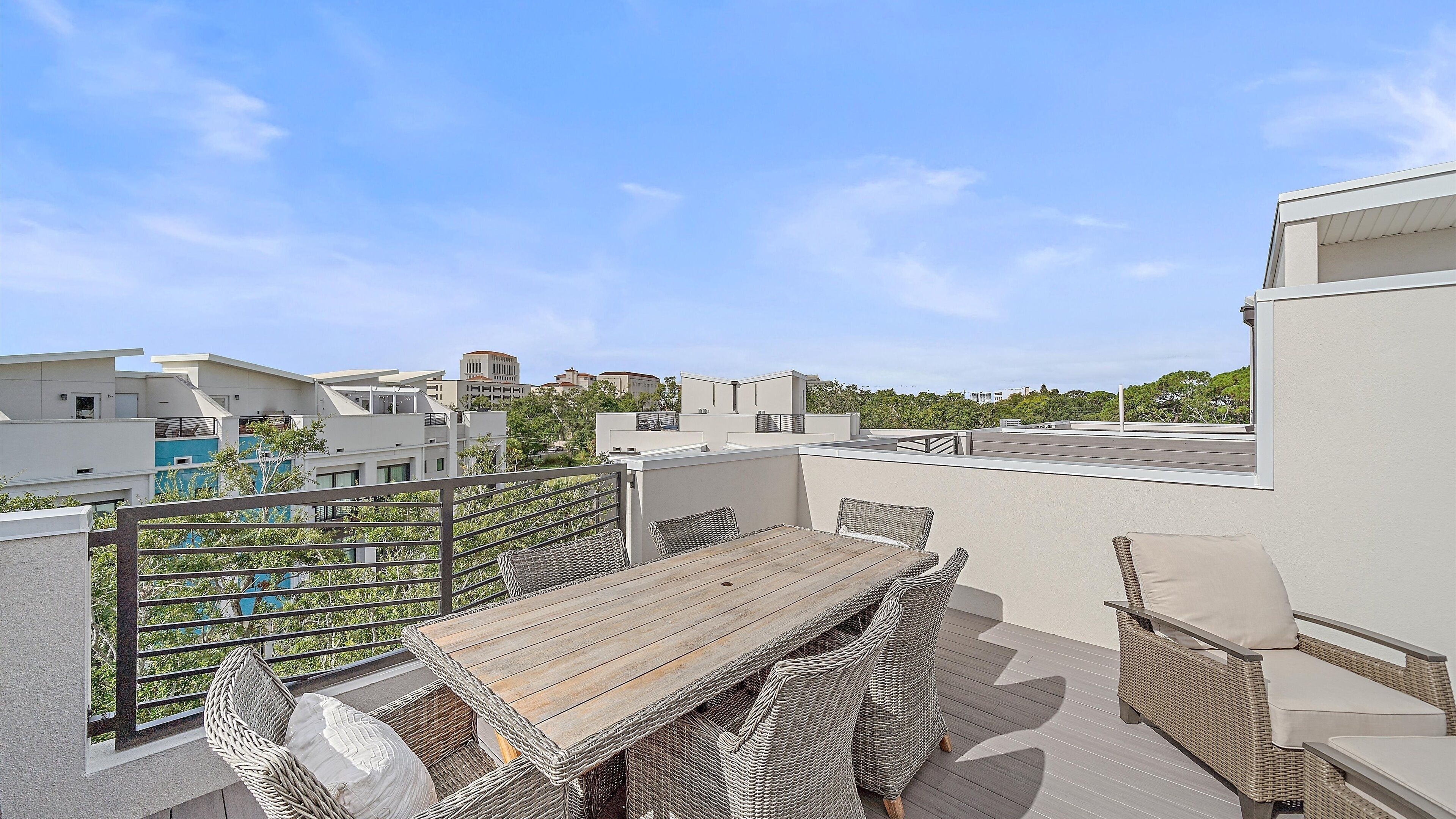 A rooftop terrace with a wooden table and wicker furniture, surrounded by a metal railing.