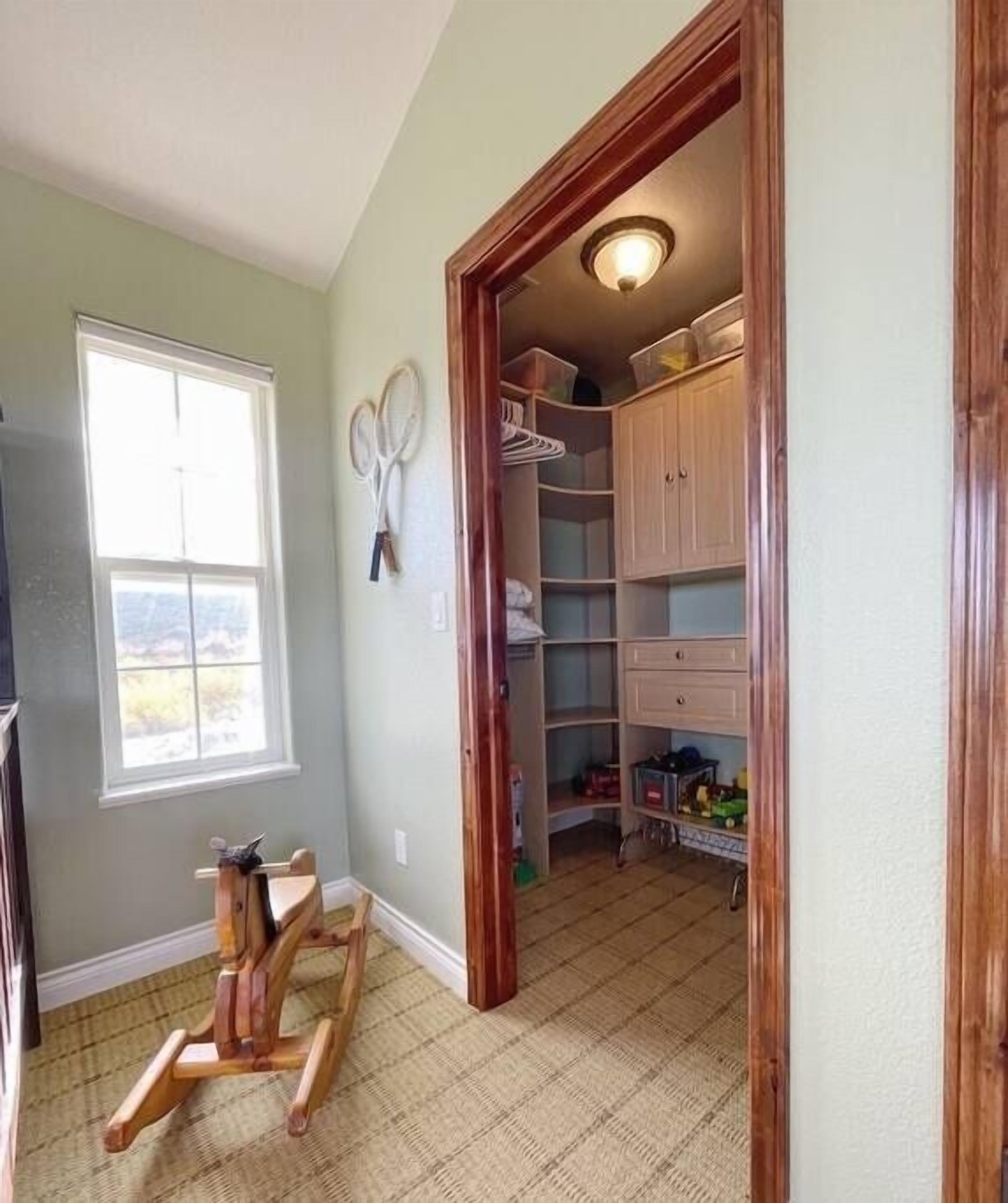 A room with a wooden rocking chair, a window with blinds, and a closet with shelves and hanging items.